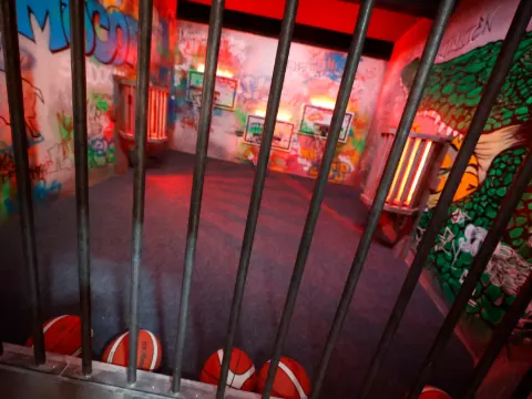 Salle graffée aux couleurs vives, vue depuis des barreaux, avec des ballons au sol