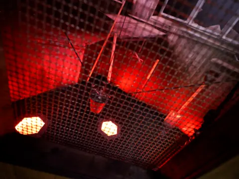 Cellule éclairée en rouge derrière un grillage, avec des cibles lumineuses au sol