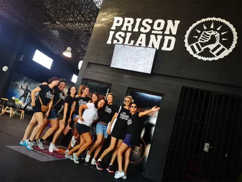 Groupe d'amis posant devant l'enseigne lumineuse Prison Island